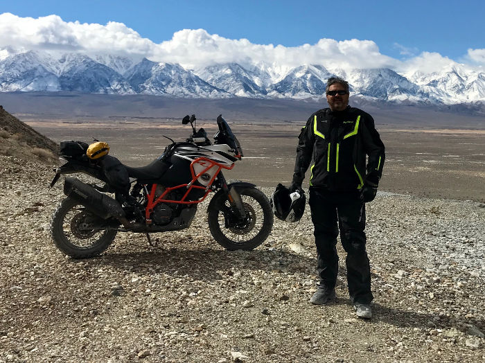 Mark Girardi standing next to motorcycle looking at mountains